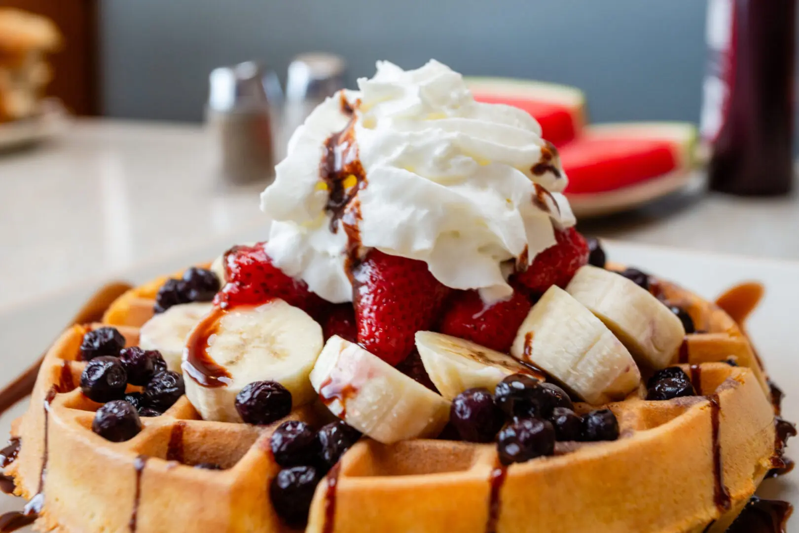 A waffle with bananas, strawberries and blueberries.